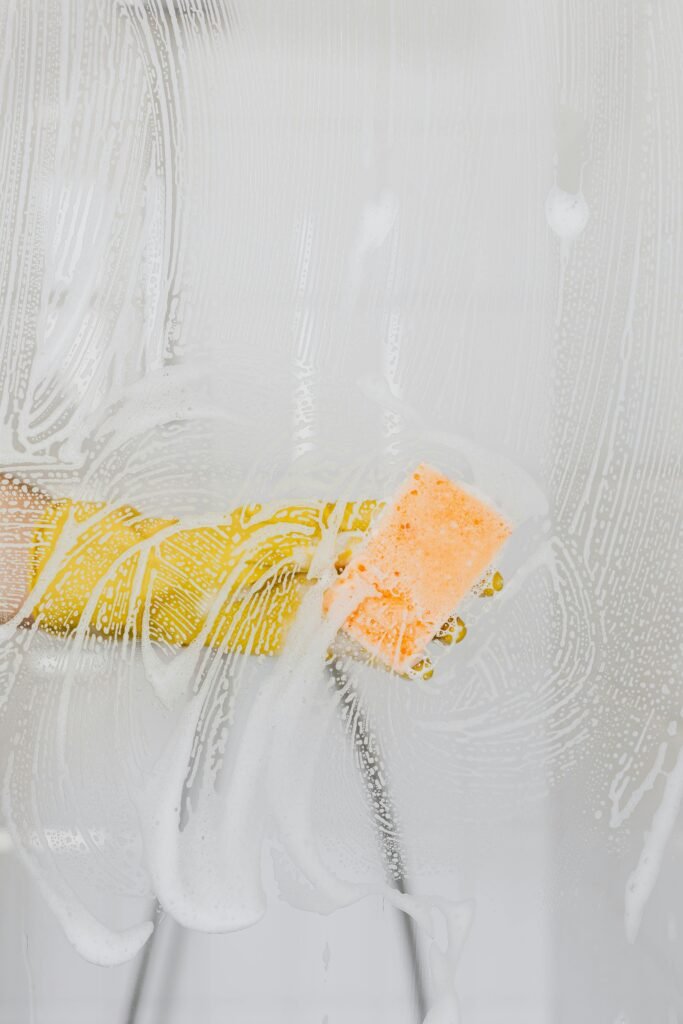 pexels-photo-4239103-4239103 A gloved hand cleans glass with a sponge and soapy water, ensuring hygiene.
